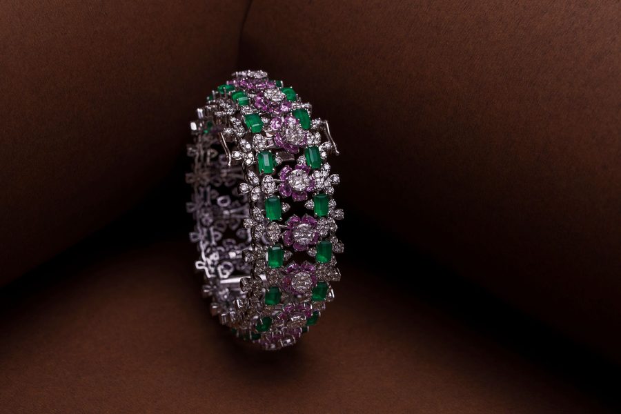 A diamond bangle set with green emeralds and pink sapphires, on warm brown velvet.