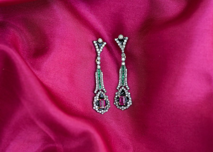 A pair of emerald and ruby drop earrings surrounded by small diamonds, resting on silk.