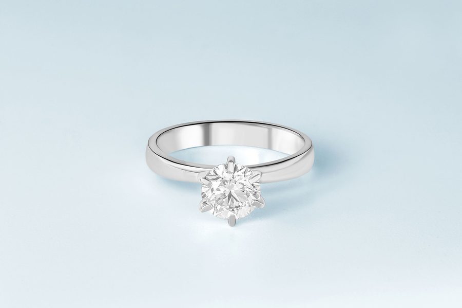 A round-brilliant diamond solitaire ring on a pale studio background.