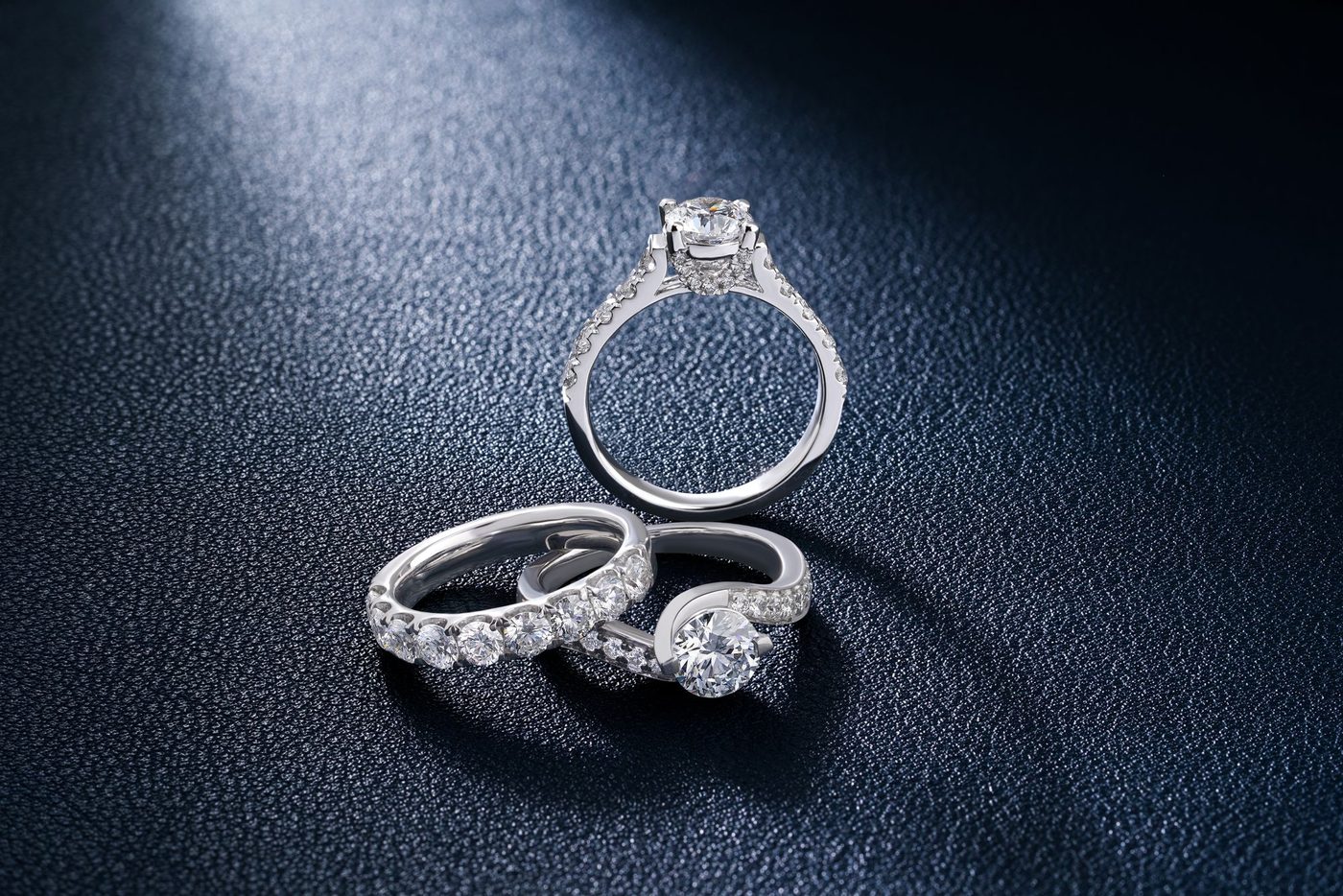 A selection of diamond rings laid out together on dark leather, the way stock is looked over before buying.
